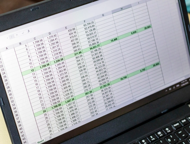 An open laptop displaying a spreadsheet with rows and columns of numerical data. Some cells are highlighted in green, indicating specific values or areas of interest. The screen is tilted slightly, showing the spreadsheet application interface.